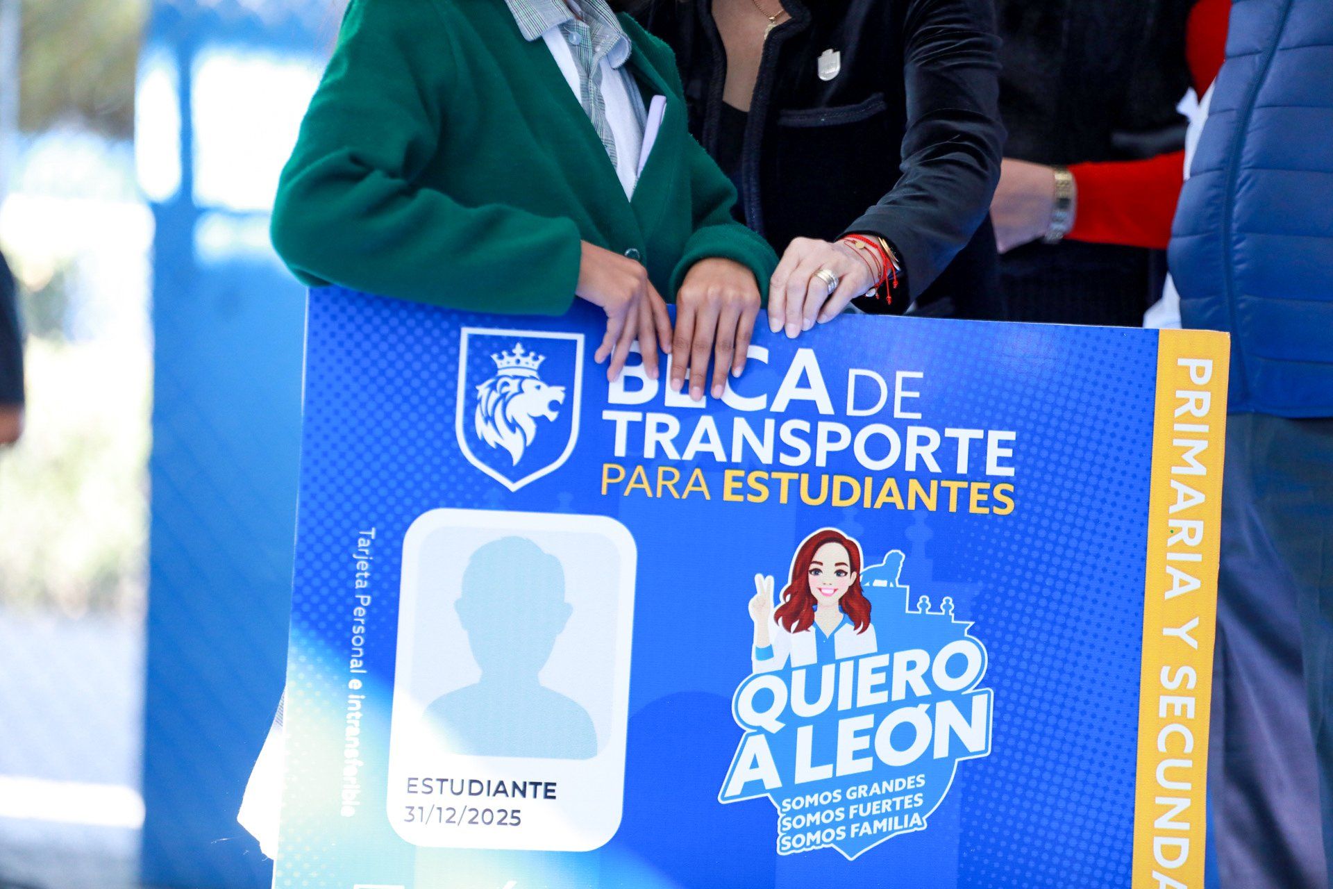 Manos sostienen una tarjeta gigante de la Beca de Transporte para Estudiantes.
