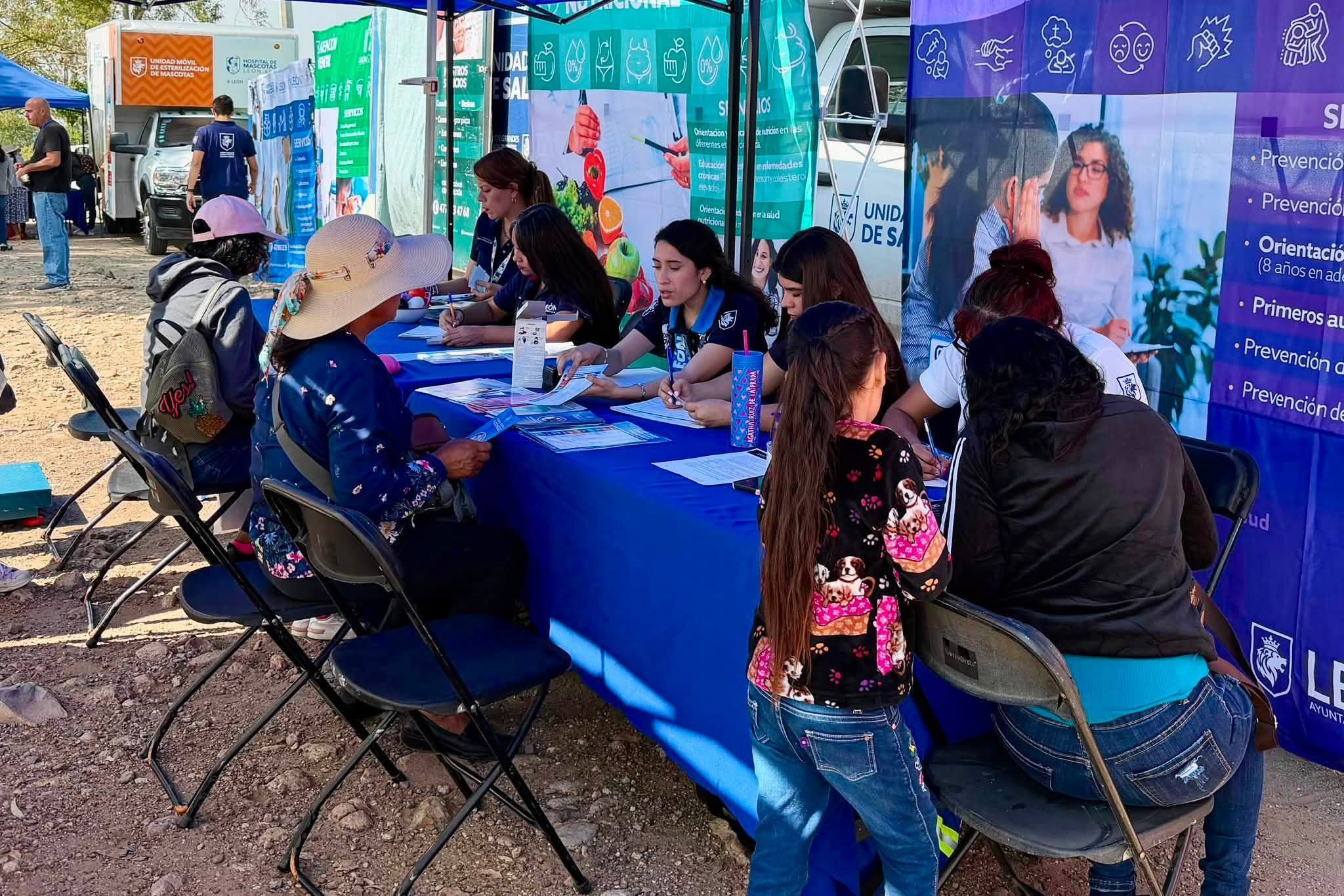 Personal de salud del Municipio atiende a vecinas y vecinos sentados en una mesa bajo un toldo.