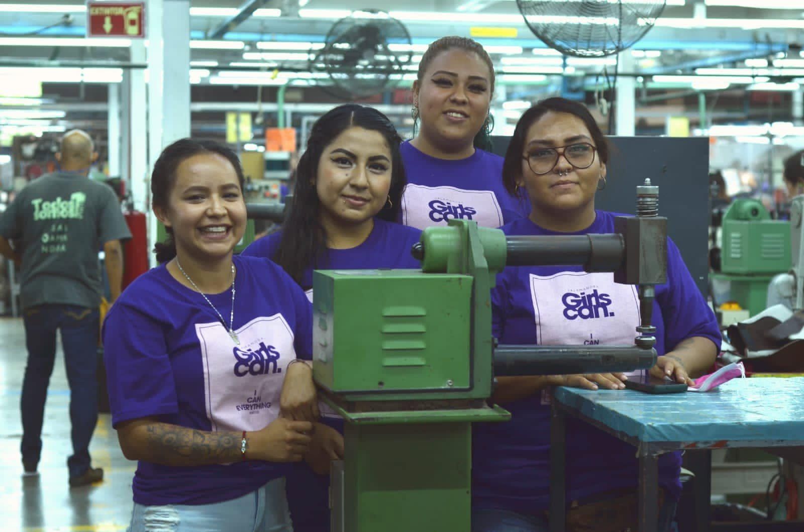 Cuatro mujeres sonríen junto a una máquina en una fábrica de calzado.